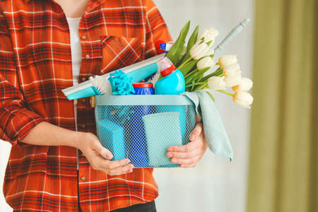 Woman with cleaning supplies and spring flowers in room, closeup