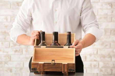 Man with bottles of wine in box on brick background