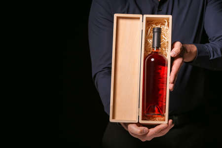 Man holding box with bottle of wine on dark backgroundの写真素材