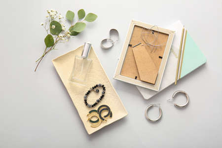 Plate with beautiful jewelry and perfume bottle on light background