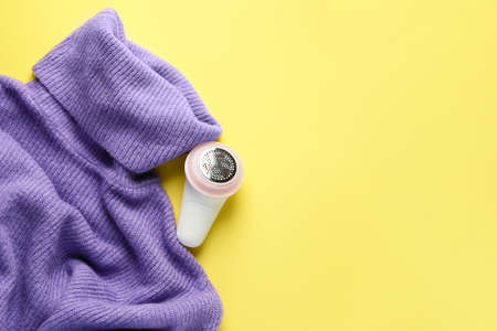 Modern fabric shaver and clothes on color background
