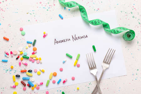 Paper sheet with text ANOREXIA NERVOSA, pills, forks and measuring tape on white backgroundの写真素材