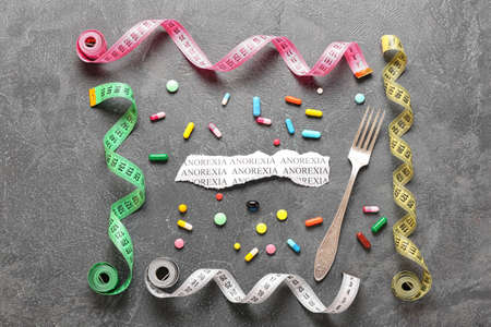 Piece of paper with text ANOREXIA, fork, pills and measuring tapes on gray backgroundの写真素材