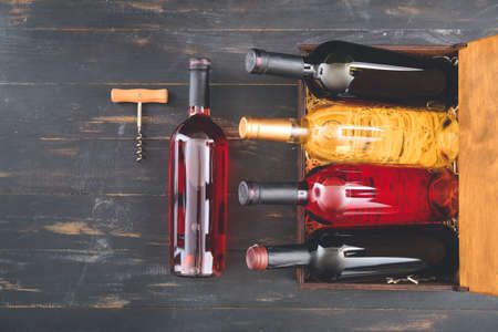 Box with bottles of wine and corkscrew on dark wooden backgroundの写真素材