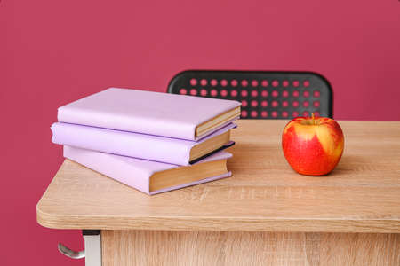 Books and apple on school desk against color backgroundの写真素材