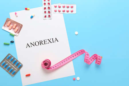 Paper sheet with text ANOREXIA, measuring tape and pills on color backgroundの写真素材