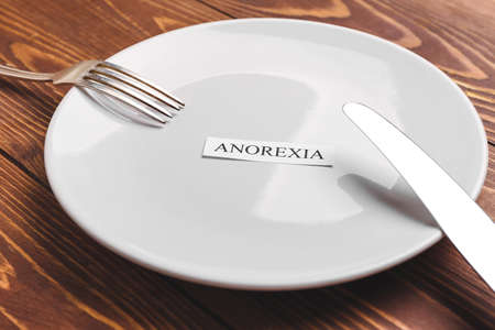 Plate and cutlery with word ANOREXIA on table