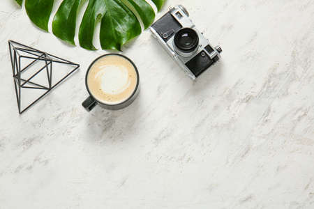 Cup of coffee, photo camera and tropical leaf on light backgroundの写真素材