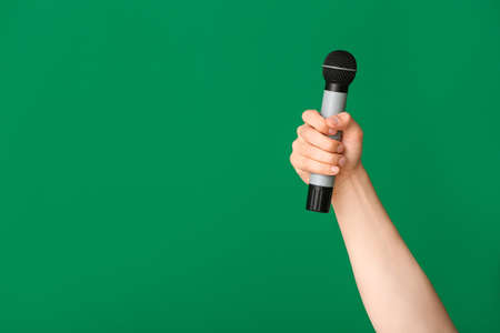 Hand of young man with microphone on color backgroundの写真素材