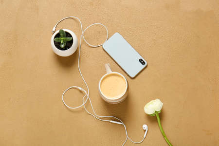 Cup of coffee, mobile phone, earphones and flower on color backgroundの写真素材