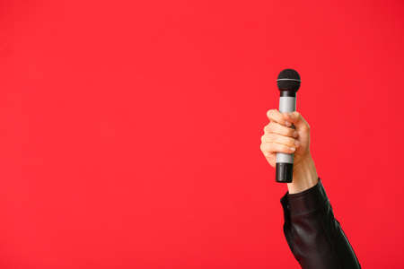 Hand of young man with microphone on color backgroundの写真素材