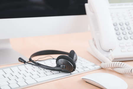 Headset and computer with telephone on table of technical support agent in officeの写真素材