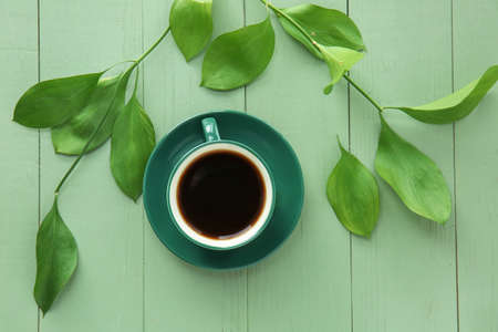 Cup of coffee and green leaves on color wooden backgroundの写真素材