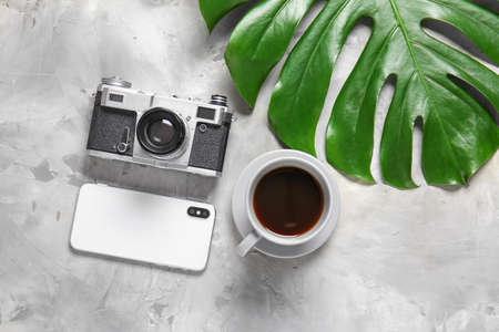 Cup of coffee, smartphone, photo camera and tropical leaf on light backgroundの写真素材