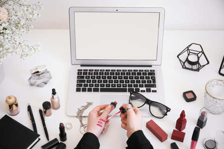 Woman with makeup cosmetics sitting at table with laptopの写真素材