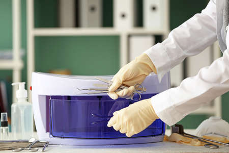 Doctor putting medical instruments into ultraviolet sterilizer in clinicの写真素材