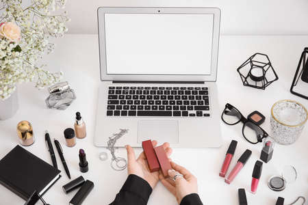 Woman with makeup cosmetics sitting at table with laptopの写真素材