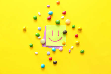 Papers with drawn happy face and candies on color backgroundの写真素材