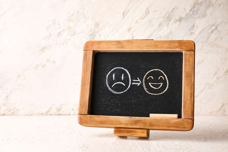 Chalkboard with drawn happy and sad faces on light backgroundの写真素材