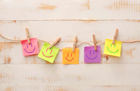 Papers with drawn happy faces on white wooden backgroundの写真素材