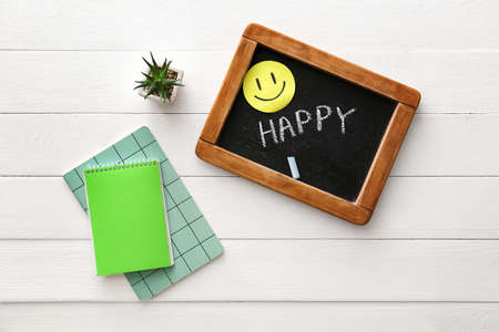 Chalkboard with word HAPPY, paper smile and notebooks on white wooden backgroundの写真素材