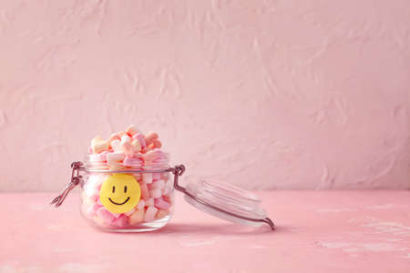 Jar with tasty marshmallows and paper smile on color backgroundの写真素材