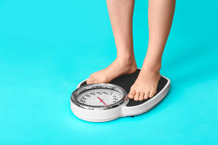 Young woman measuring her weight against color backgroundの写真素材