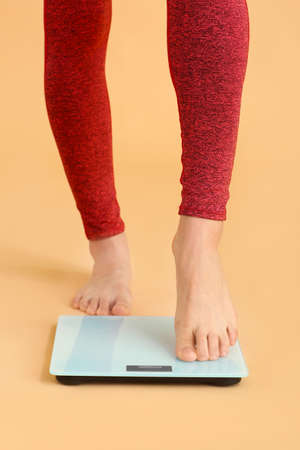 Young woman measuring her weight on color background