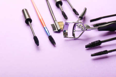 Mascara and eyelash curler on color background