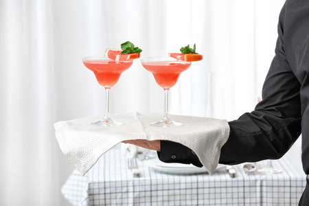 Waiter with glasses of tasty mimosa cocktail on tray at banquet