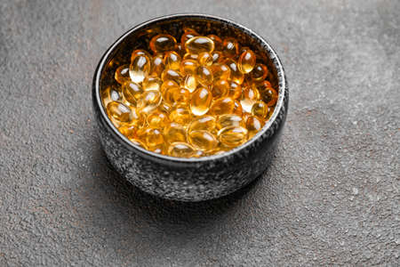 Bowl with fish oil capsules on gray backgroundの写真素材