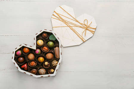 Heart-shaped box with delicious candies on white background