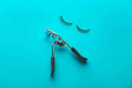 Fake eyelashes and curler on color background