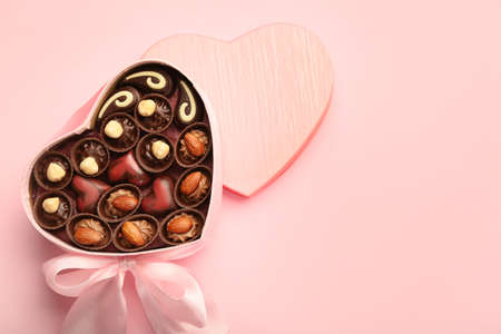 Heart-shaped box with chocolate candies on color backgroundの写真素材