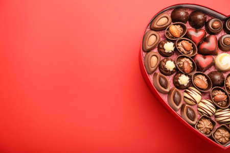 Heart-shaped box with chocolate candies on color background