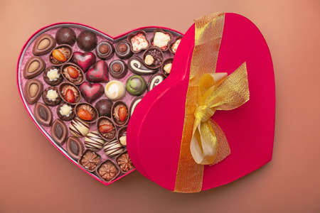 Heart-shaped box with chocolate candies on color background