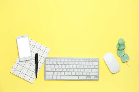 Computer keyboard with notebook and mobile phone on color background