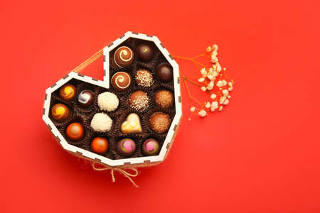 Heart-shaped box with chocolate candies and flowers on color backgroundの写真素材