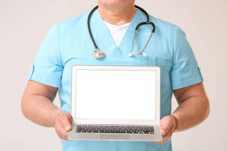 Mature male doctor with laptop on gray backgroundの写真素材