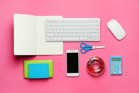 Computer keyboard with stationery and mobile phone on color background
