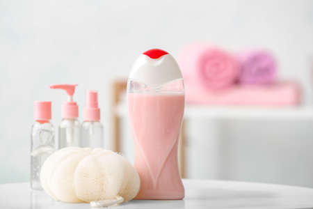 Different shower gels and loofah on table in bathroom