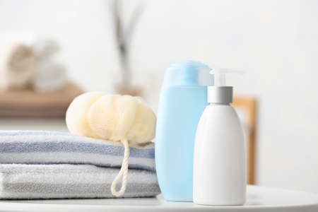 Different shower gels, towel and loofah on table in bathroom