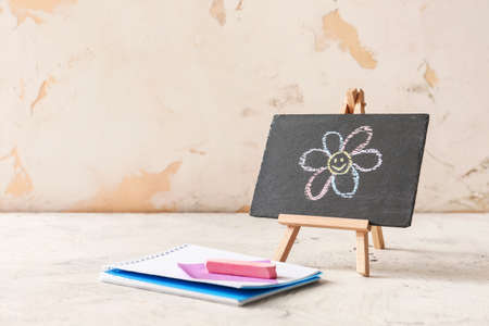 Chalkboard with drawn flower and notebook on white backgroundの写真素材