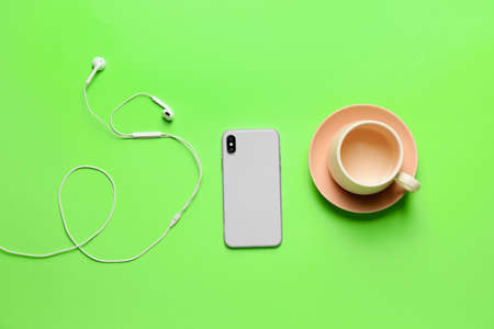 Empty cup, mobile phone and earphones on color backgroundの写真素材