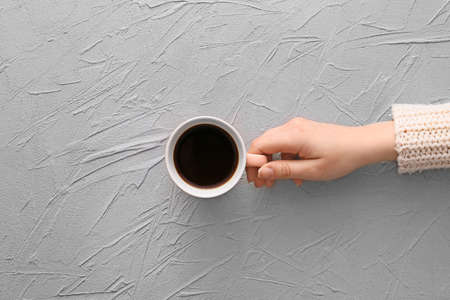 Female hand with cup of hot coffee on gray background, top view