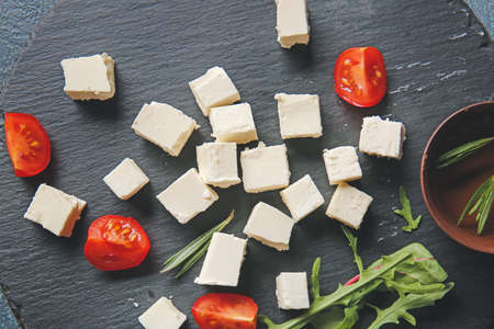 Slate plate with tasty cut feta cheese, tomatoes and herbs on tableの写真素材