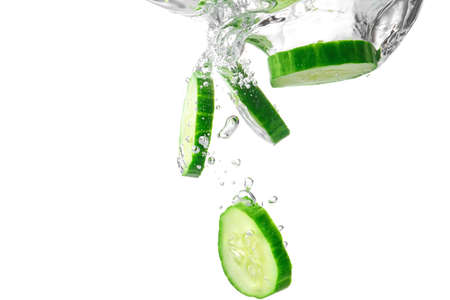 Falling of fresh cucumber slices into water against white backgroundの写真素材