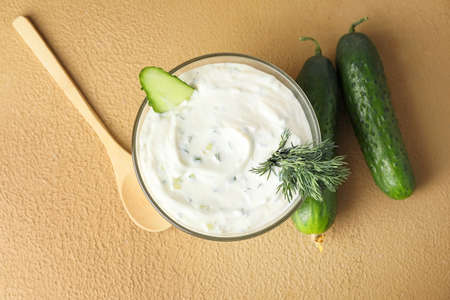 Delicious yogurt sauce with cucumber in bowl on color background