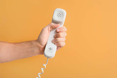 Male hand with corded phone on color background
