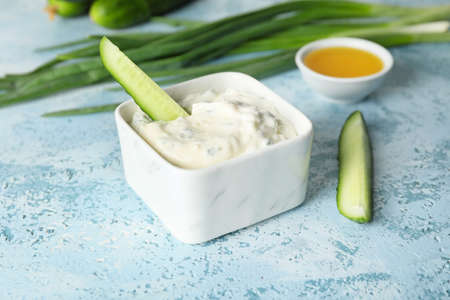 Delicious yogurt sauce with cucumber in bowl on color backgroundの写真素材